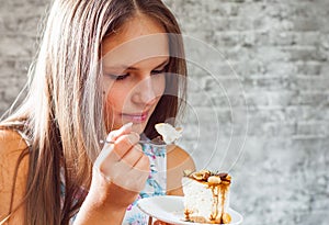 Young teenager brunette girl with long hair eating cake dessert on gray wall background