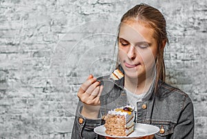 Young teenager brunette girl with long hair eating slice cake dessert on gray wall background