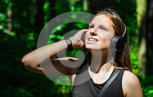 Portrait of young teenager brunette girl with long hair. Happy young woman listening to music with headphones in forest.