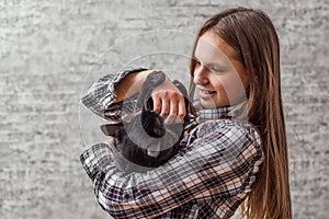 Portrait of young teenager brunette girl with long hair holding in her arms black cat on gray wall background