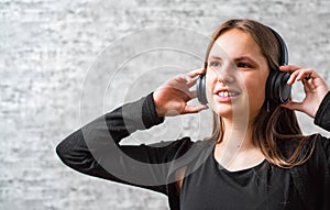 Portrait of young teenager brunette girl with long hair listening music on wireless headphones