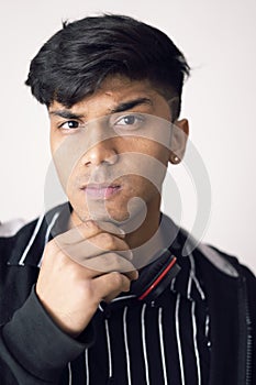 Portrait of young teenager resting chin on fist, clean shave and wearing black jacket against white background