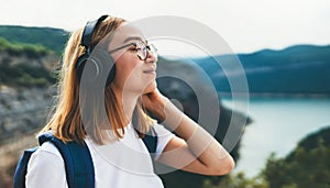 Portrait of young tourist woman with long hair wearing hipster glasses listening to favorite music on headphones smiling