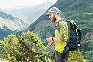 Portrait of a young traveler with a beard and a backpack in a cap and sunglasses against the background of the Caucasus