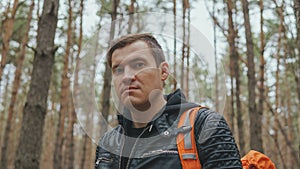 Portrait of young traveling man in woods. Close up of adult male in leather jacket with backpack in forest.