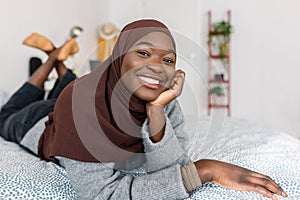 Portrait of young trendy african woman in muslim headscarf lying on bed