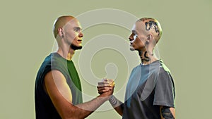 Portrait of young twin brothers with tattoos and piercings looking at each other, holding hands, standing face to face