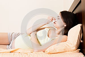 Portrait of young unhappy pregnant woman leaning on pillows on bed and blowing her nose into tissue. Future mom caught cold and