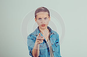 Portrait young; unhappy; serious woman pointing finger at someone; blaming for something wrong; mistake; isolated green grey