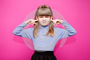 Portrait of young unhappy, stressed little girl covering her ears with fingers calling to stop noise isolated on pink