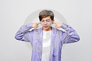 Portrait of young upset boy 12-14 years covering ears, asking for silence. Child on grey background