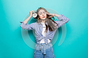 Portrait of young upset puzzled woman student in denim clothes hold alarm clock isolated on blue background. Time is running out.