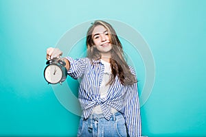 Portrait of young smile puzzled woman student in denim clothes hold alarm clock isolated on blue background. Time is running out.