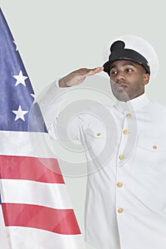 Portrait of a young US Navy officer saluting American flag over gray background