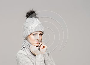 Portrait of a young and beautiful woman in a winter hat over grey background.