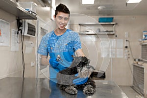 Portrait of young veterinarian technician in medical uniform with happy dog after ears check