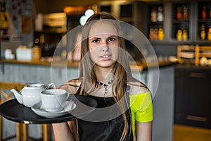 Portrait young waitress standing in cafe. girl the waiter holds in bunches a tray with utensils