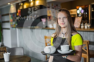 Portrait young waitress standing in cafe. girl the waiter holds in bunches a tray with utensils