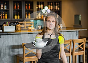 Portrait young waitress standing in cafe. girl the waiter holds in bunches a tray with utensils