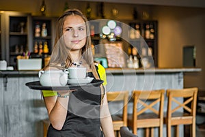 Portrait young waitress standing in cafe. girl the waiter holds in bunches a tray with utensils.