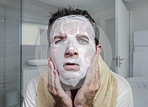 Portrait of young weird and funny man at home trying using beauty paper facial mask cleansing learning anti aging treatment in