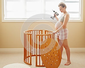 Portrait of young white Caucasian happy woman assembling wooden baby crib in nursery at home