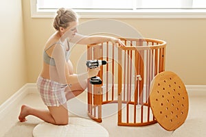 Portrait of young white Caucasian happy woman assembling wooden baby crib in nursery at home