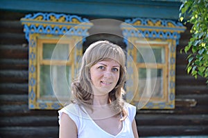 Portrait of the young woman against the wooden house with carved platbands