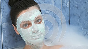 Portrait of young woman with alginate mask lying in bathroom with foam at home.