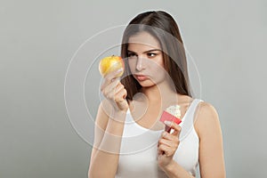 Portrait of young woman with apple and a tasty cupcake, choosing healthy food or dessert