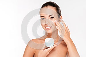 Portrait of young woman applying moisturizer cream on her face