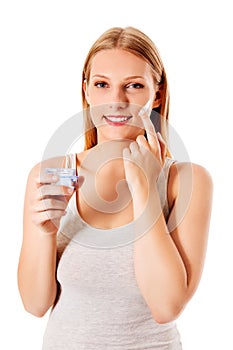 Portrait of young woman applying moisturizer cream on her pretty face
