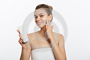 Portrait of young woman applying moisturizer cream on her pretty face. Isolated on white background