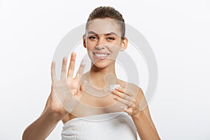 Portrait of young woman applying moisturizer cream on her pretty face. Isolated on white background