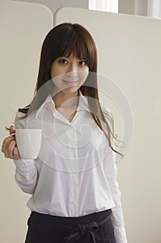Portrait of young woman with apron holding a cup of coffee