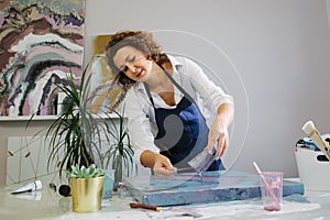 Portrait of a young woman artist in studio, working with acrylic paints on canvas. Fluid art.