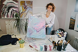 Portrait of a young woman artist in studio, working with acrylic paints on canvas. Fluid art.