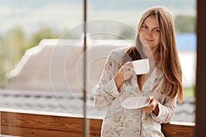 Portrait of young woman on the balcony holding a cup of coffee or tea in the morning