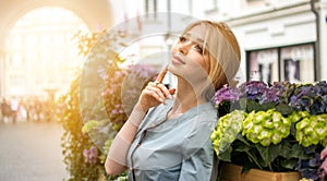 Portrait of young woman with beautiful face like a doll looking away while leaning over flower terrace.