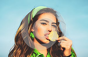 Portrait of young woman, beautiful lips, bright make-up holding, eating fried potato, fries, chips and posing over blue