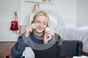 Portrait of young woman, beauty content creator, sitting in a room in front of digital camera, recording makeup tutorial