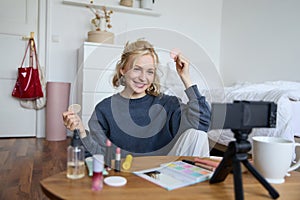 Portrait of young woman, beauty content creator, sitting in a room in front of digital camera, recording makeup tutorial