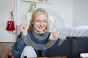 Portrait of young woman, beauty content creator, sitting in a room in front of digital camera, recording makeup tutorial