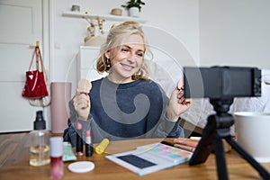 Portrait of young woman, beauty content creator, sitting in a room in front of digital camera, recording makeup tutorial