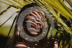 Portrait of young woman behind palm leaves. Exotic tropical leaves near her face. Beauty, fashion, cosmetology, nature