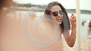 Portrait of young woman in bikini sitting with friends on the beach and smiling.