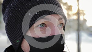 Portrait of a young woman in a black mask stands in the city in the winter. Woman wearing protective medical mask