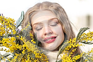 Portrait of a young woman with blond hair holding a bouquet of mimosa in her hands. Spring