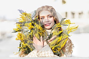 Portrait of a young woman with blond hair holding a bouquet of mimosa in her hands. Spring