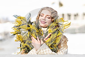 Portrait of a young woman with blond hair holding a bouquet of mimosa in her hands. Spring